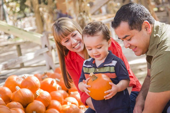 Happy family with young boy holding and choosing a pumpkin