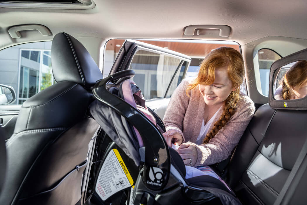 Mother strapping baby in car seat.
