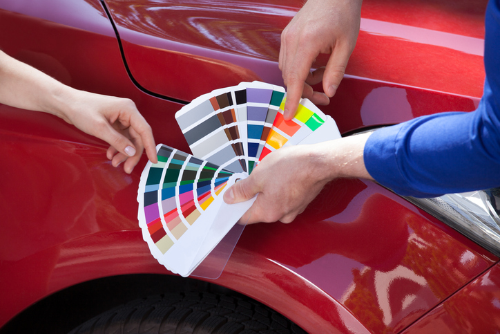 Cropped image of mechanic showing color samples to customer against car